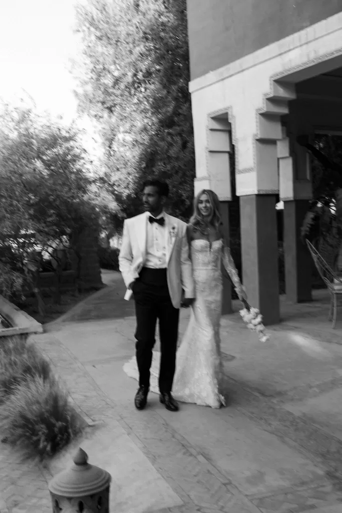 Black and white candid of the bride and groom walking hand in hand through Beldi Country Club’s gardens.
