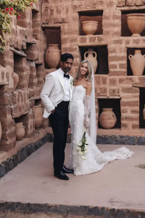 Bride and groom standing against a rustic clay wall with terracotta vases at Beldi Country Club.