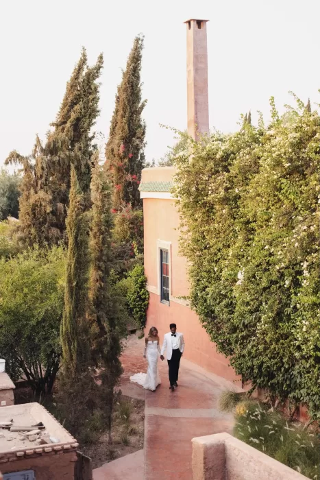 Bride and groom strolling hand in hand along a terracotta pathway surrounded by greenery at Beldi Country Club.