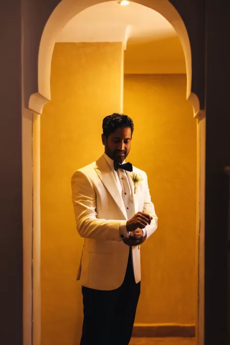 Groom adjusting his cufflinks in a warm arched hallway at Beldi Country Club.