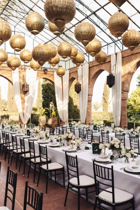 Elegant wedding reception at Beldi Country Club with long banquet tables, white linens, and golden Moroccan lanterns overhead.