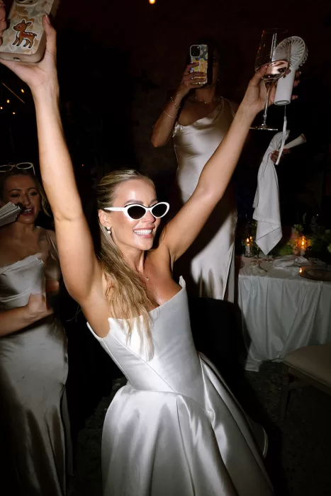 Bride in sunglasses dancing with arms raised during lively reception at Cases de Sa Fonseca.