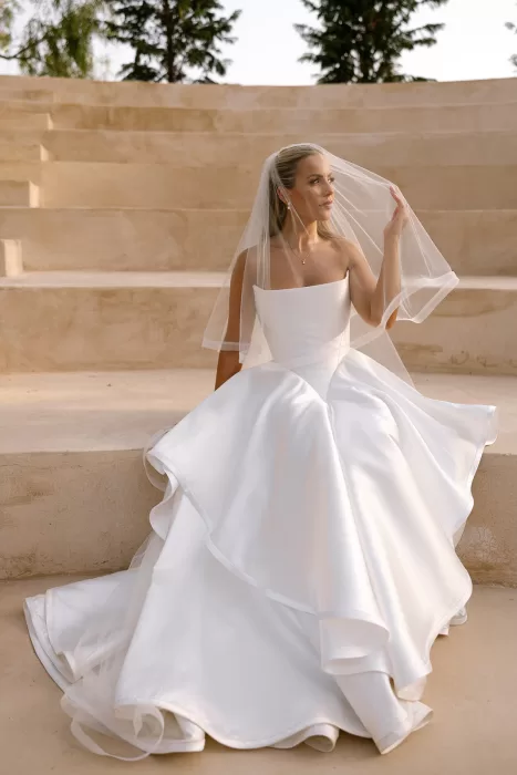 Bride in a flowing white gown and veil seated on stone steps at Cases de Sa Fonseca amphitheater.