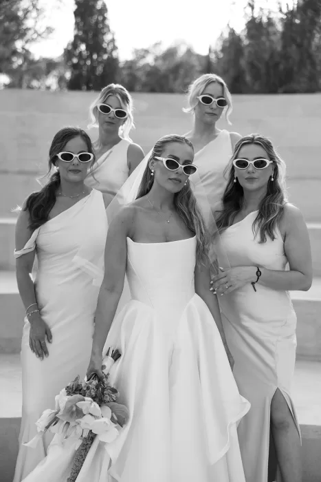 Bride and bridesmaids in chic white gowns and sunglasses posing with confidence at Cases de Sa Fonseca.