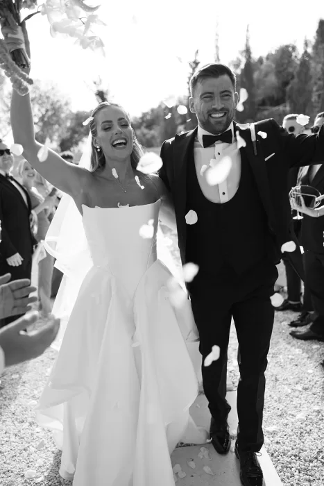 Black and white photo of bride and groom celebrating joyfully as petals fall at Cases de Sa Fonseca wedding.