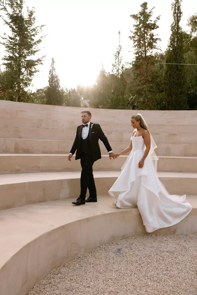 Bride and groom holding hands as they walk along the amphitheater steps at Cases de Sa Fonseca.