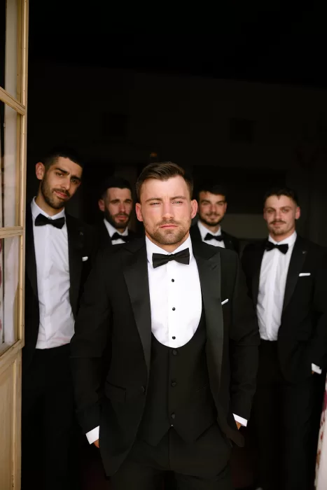 Groom with groomsmen in black tie suits standing confidently in a doorway at Cases de Sa Fonseca.
