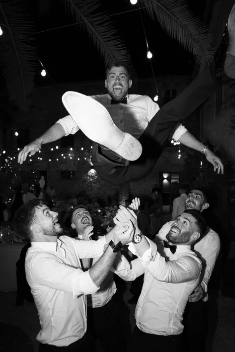 Guests joyfully toss the groom into the air during wedding celebrations at Cases de Sa Fonseca.