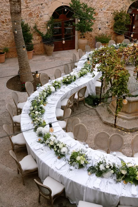 Wedding reception tables at Cases de Sa Fonseca styled with white linens and lush green and white floral arrangements.