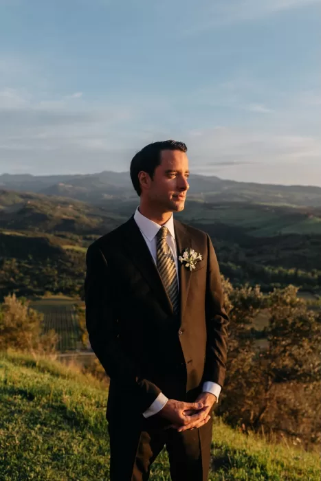 Groom portrait at Castello di Velona during golden hour with Tuscan hills behind.