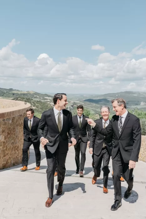 Groom walking with groomsmen in black suits at Castello di Velona, Tuscany.