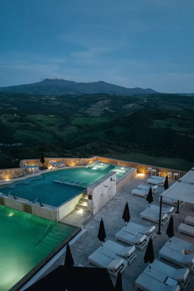 Illuminated infinity pools at Castello di Velona with panoramic Tuscan valley views at dusk.