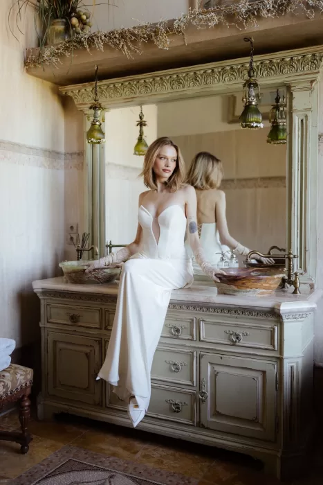 Bride in strapless gown sitting on vintage dresser with mirror in Chateau Challain suite.