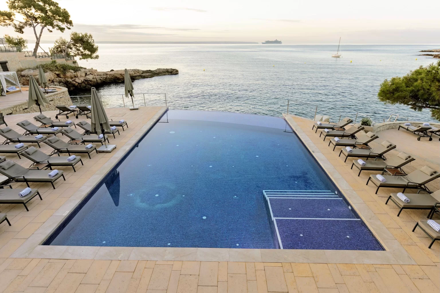 Infinity pool at Hospes Maricel & Spa at sunset with loungers and expansive sea view.