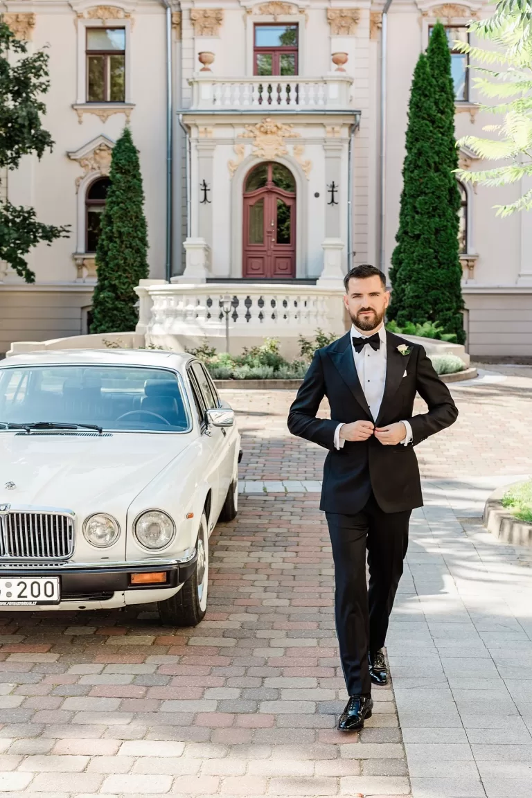 Black and white portrait of groom in suit standing in a colonnade, captured by Jurgita Lukos.