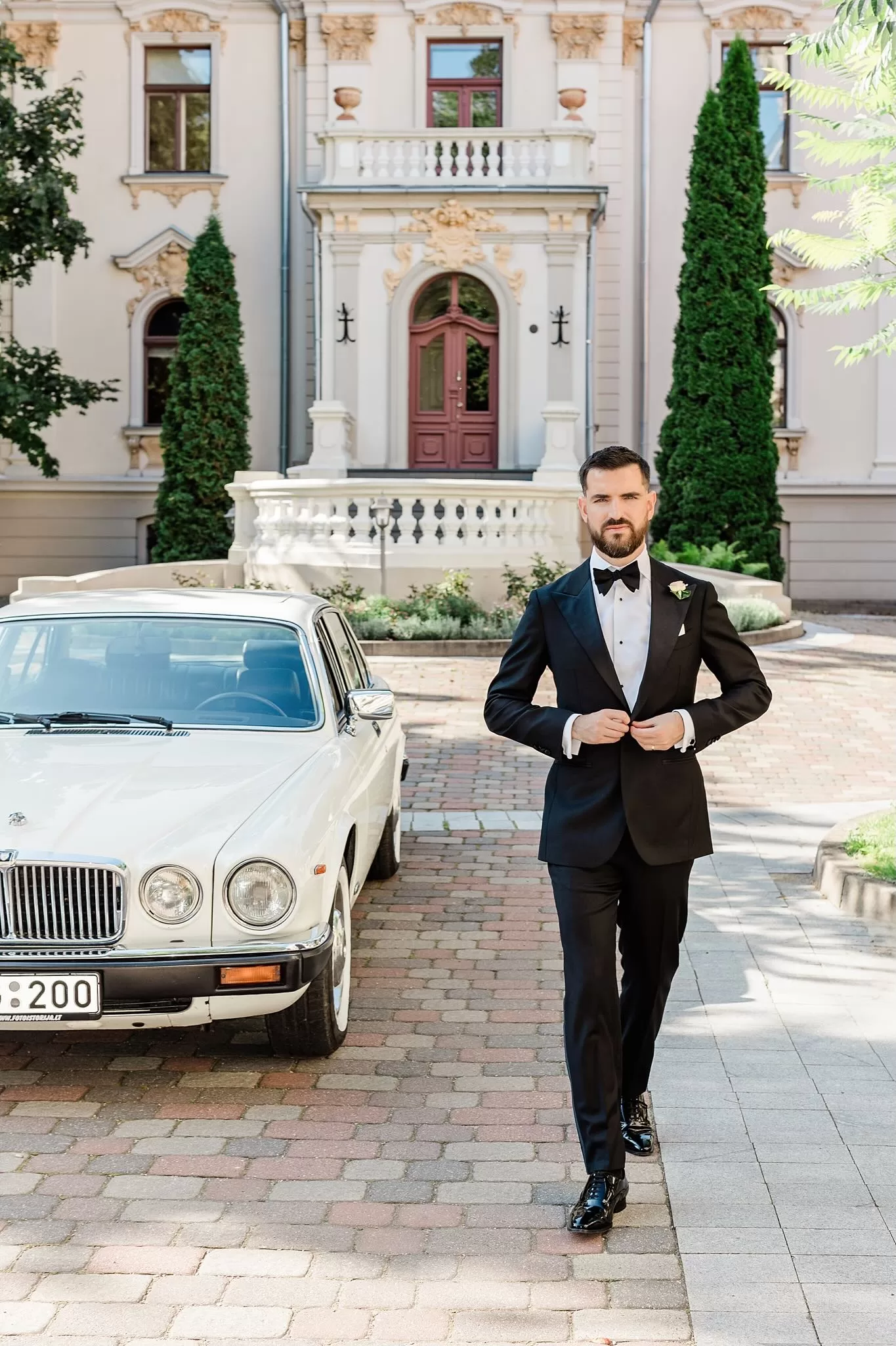 Black and white portrait of groom in suit standing in a colonnade, captured by Jurgita Lukos.