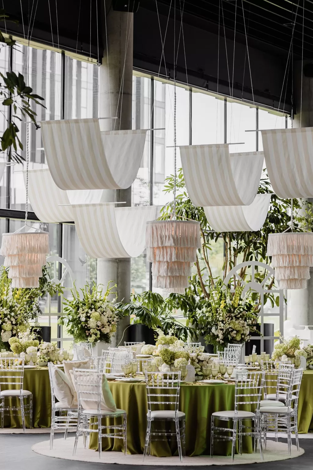 Elegant wedding reception with green table linens, floral arrangements, and modern hanging drapes, by Jurgita Lukos.