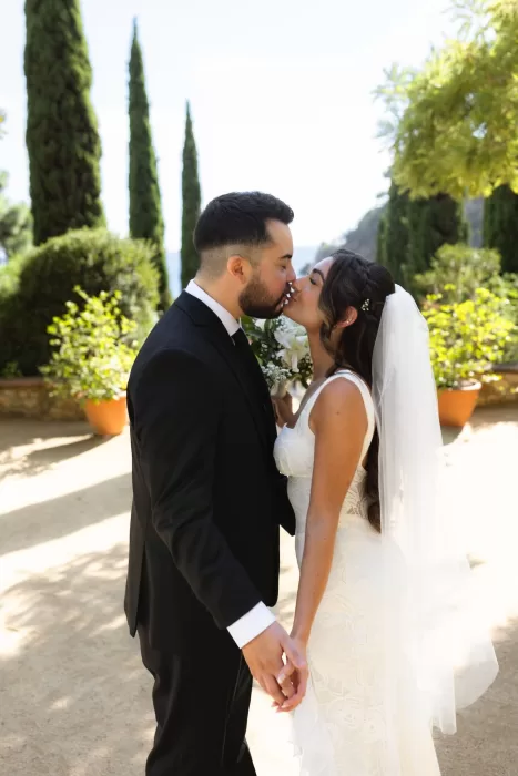 Bride and groom kissing along a sunlit garden path at Marimurtra Botanical Garden.