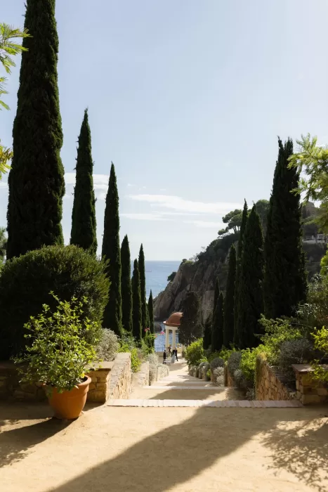 Tree-lined stone pathway leading to the seaside pavilion at Marimurtra Botanical Garden.