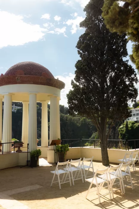 White chairs arranged for a seaside wedding ceremony by the pavilion at Marimurtra Botanical Garden.