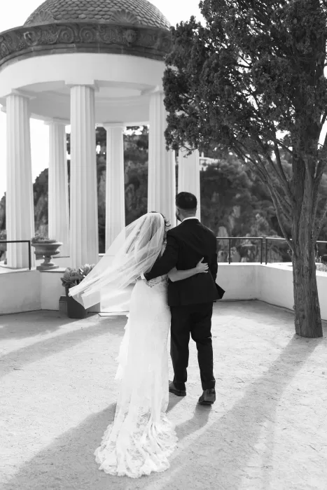 Bride and groom walking arm in arm beneath the classical pavilion at Marimurtra Botanical Garden.
