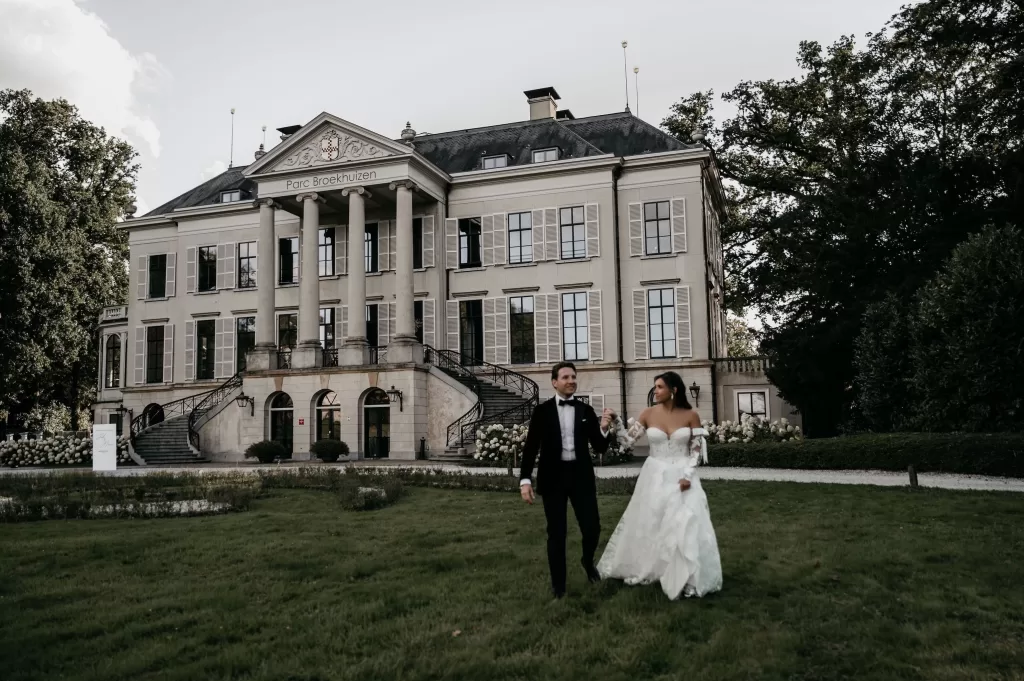 Bride and groom walking hand in hand across the gardens of Parc Broekhuizen.