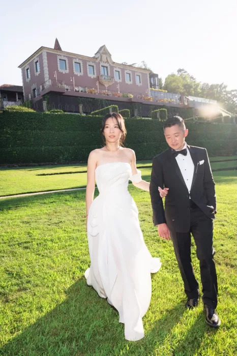 Bride and groom walking across sunlit lawn in front of Six Senses Douro Valley.