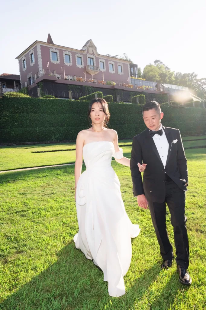 Bride and groom walking across sunlit lawn in front of Six Senses Douro Valley.