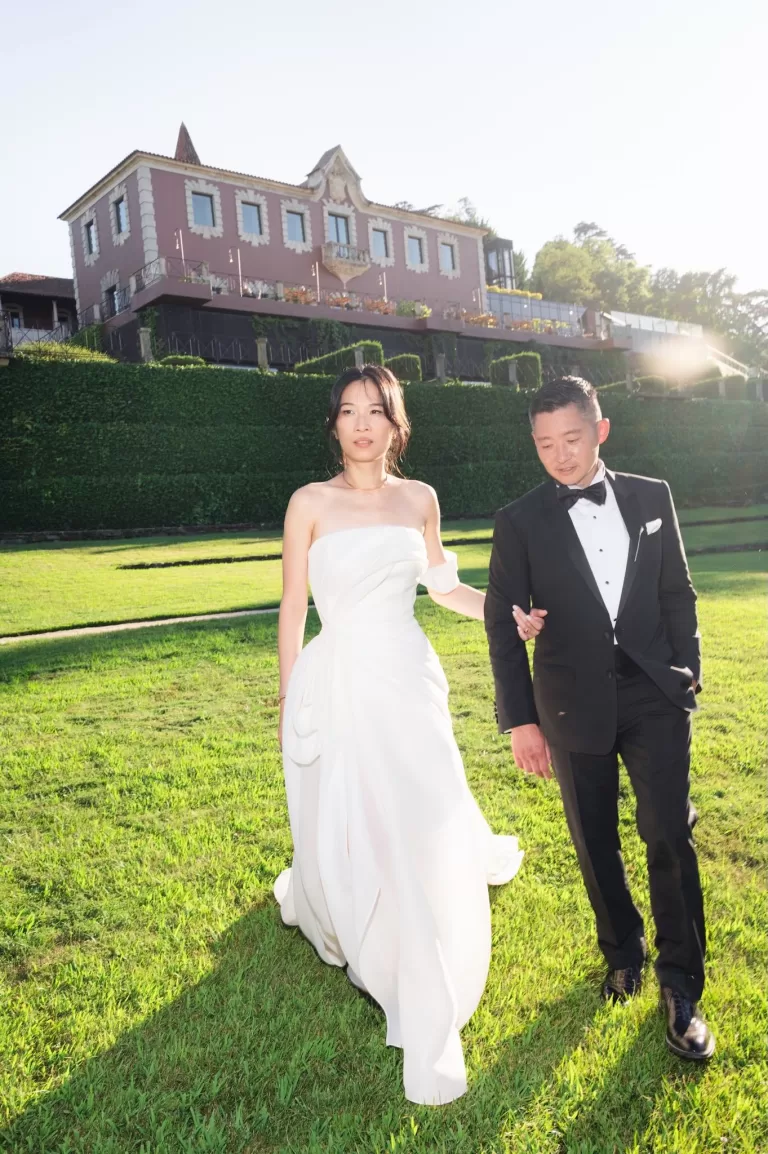 Bride and groom walking across sunlit lawn in front of Six Senses Douro Valley.