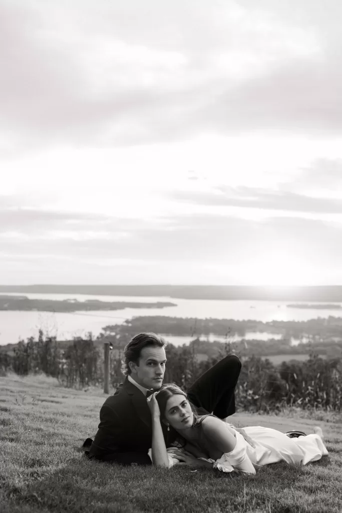 Bride resting her head on the groom’s chest as they lie on the grass overlooking the Stone Haven landscape.