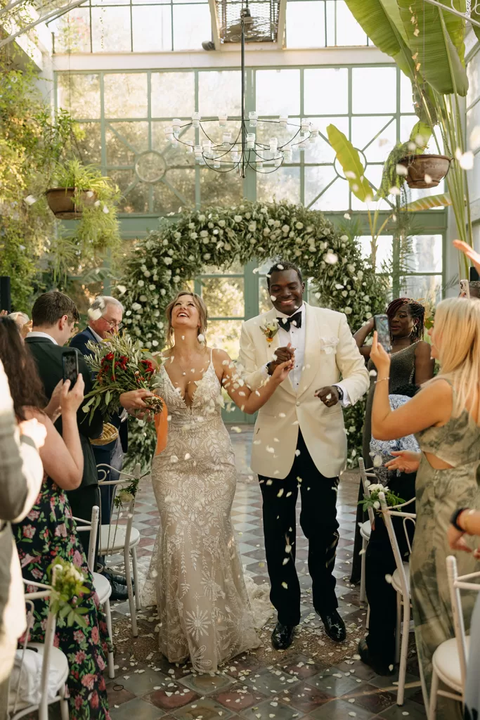 Joyful couple walking down the aisle as petals fall around them after their ceremony at Beldi Country Club.