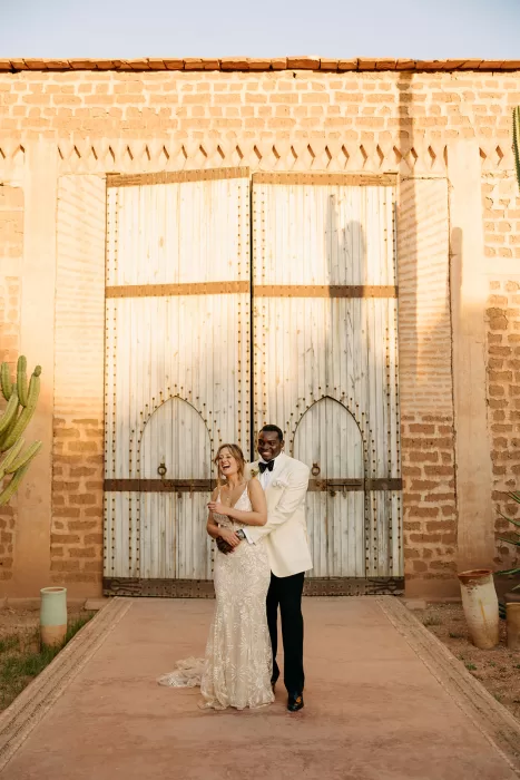 Bride and groom embracing in front of sunlit wooden doors in the courtyard of Beldi Country Club.