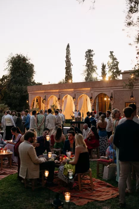 Guests enjoying an outdoor cocktail reception at dusk at Beldi Country Club, surrounded by candlelight and soft draping.