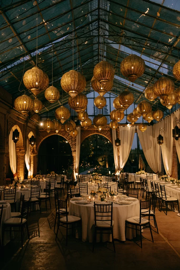 Romantic evening reception at Beldi Country Club with glowing lanterns and candlelit round tables under a glass canopy.