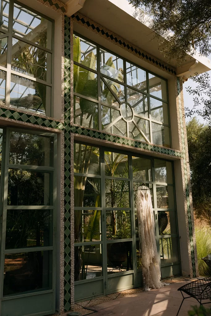 Exterior of the glasshouse at Beldi Country Club with green framed windows and a wedding dress hanging in the sunlight.