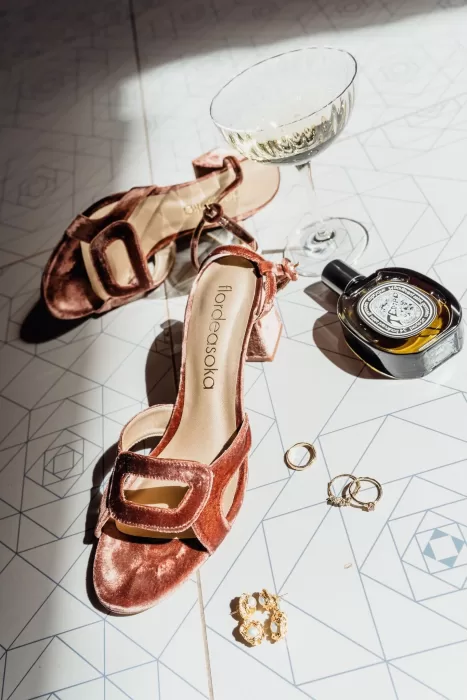 Velvet wedding shoes, gold jewelry, and perfume arranged stylishly on patterned tiles at This Must Be The Place.