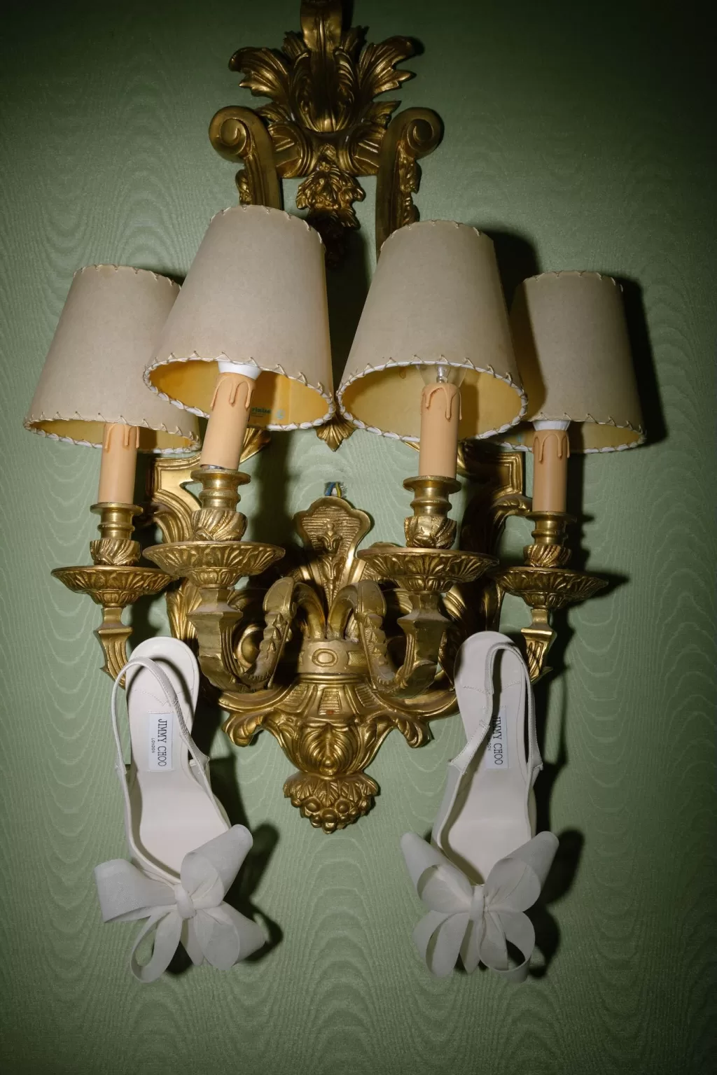 Artistic flat lay of Jimmy Choo bridal heels hanging from a vintage gold wall sconce, photographed by Abraham Garcia.