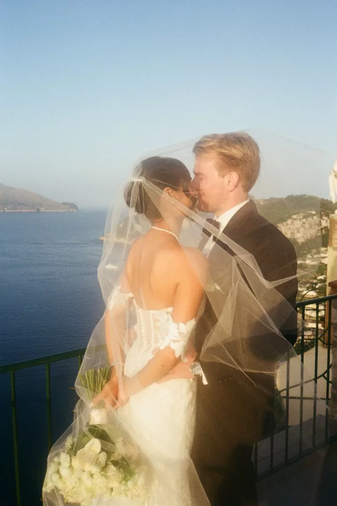 Romantic moment as newlyweds share a kiss under the bride’s veil on the balcony of Caesar Augustus Capri overlooking the sea at sunset.