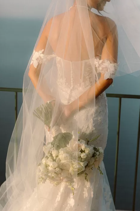 Bride holding a white rose bouquet under a sheer veil on the terrace of Caesar Augustus Capri at golden hour.
