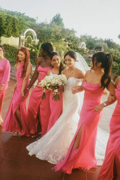 Bride walking arm in arm with bridesmaids in fuchsia dresses at Caesar Augustus Capri, surrounded by lush gardens.