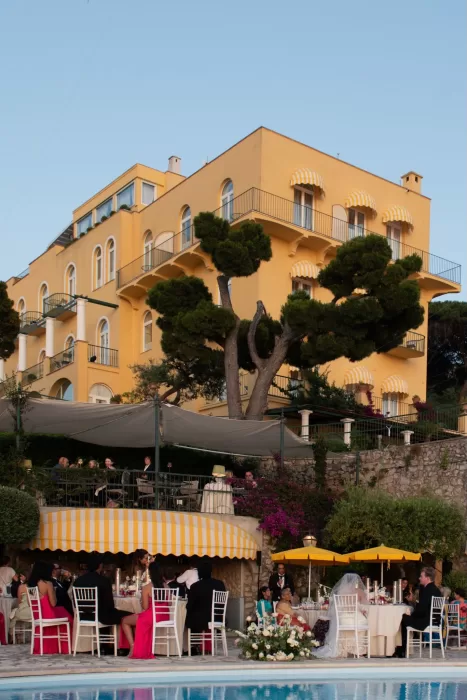 Elegant evening dinner at Caesar Augustus Capri with guests dining beside the pool and yellow-striped awnings.
