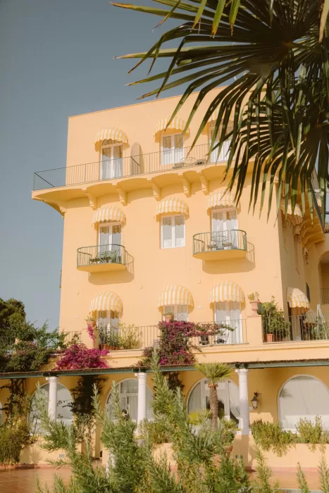 Iconic yellow exterior of Caesar Augustus Capri with striped awnings, lush bougainvillea, and sunlit balconies.