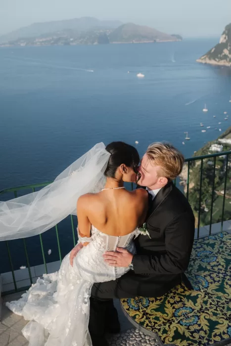Bride and groom sharing a kiss on the terrace of Caesar Augustus Capri with panoramic sea views behind them.