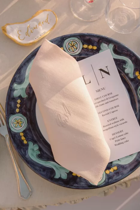 Elegant wedding table setting at Caesar Augustus Capri with hand-painted Italian plate, monogrammed napkin, and custom oyster shell place card in the soft afternoon light.