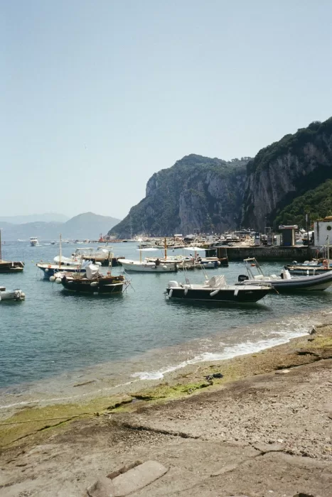 Boats floating in the crystal waters of Capri’s marina beneath rugged limestone cliffs.
