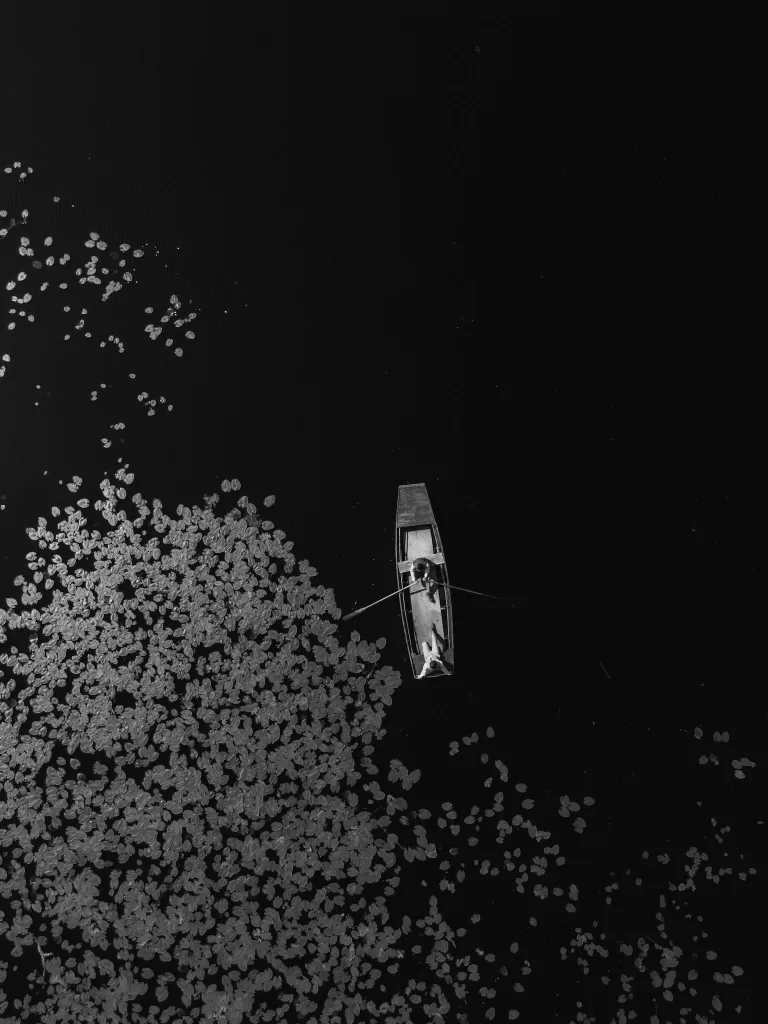 Aerial view of a couple rowing across the lily-covered lake at Château de Pordor, captured in timeless black and white.