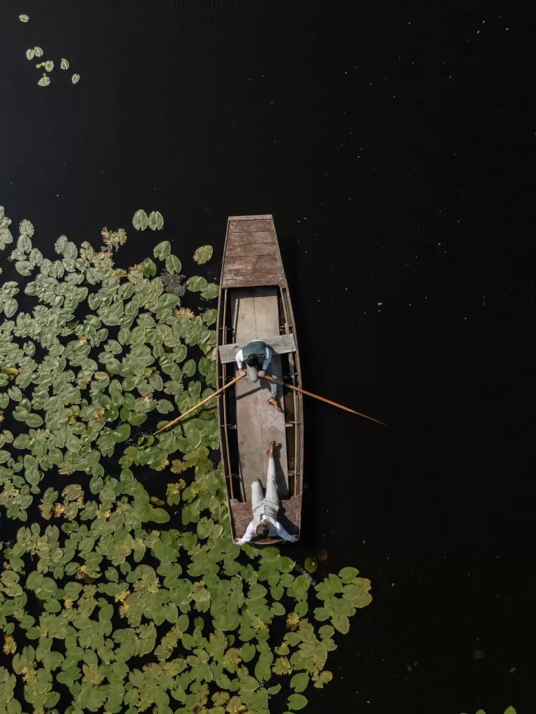 Aerial view of the grooms relaxing in a wooden rowboat among lily pads on the lake at Château de Pordor.
