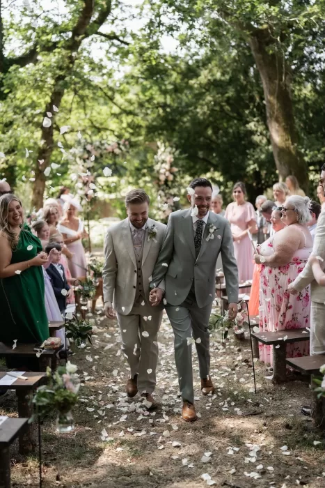 The newlyweds walking hand in hand down the aisle as guests throw petals during their outdoor ceremony at Château de Pordor.