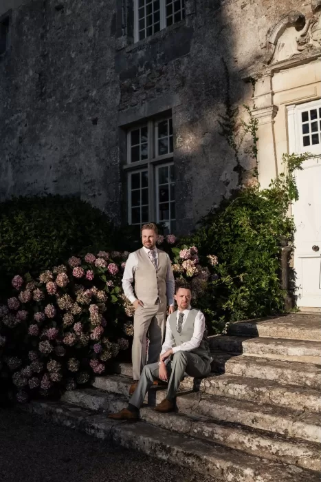 The grooms on the château steps framed by pink hydrangeas and golden evening light at Château de Pordor