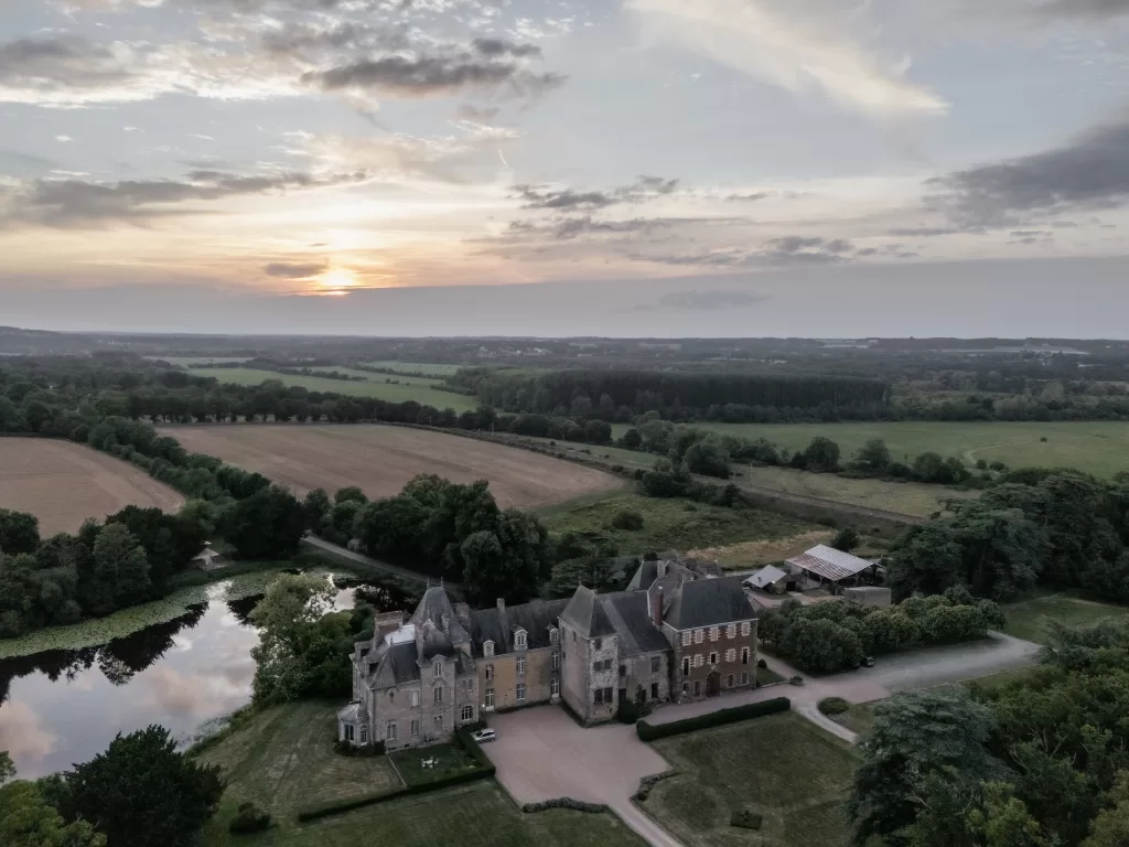 Aerial view of Château de Pordor at dusk, surrounded by serene countryside and reflective lake views.